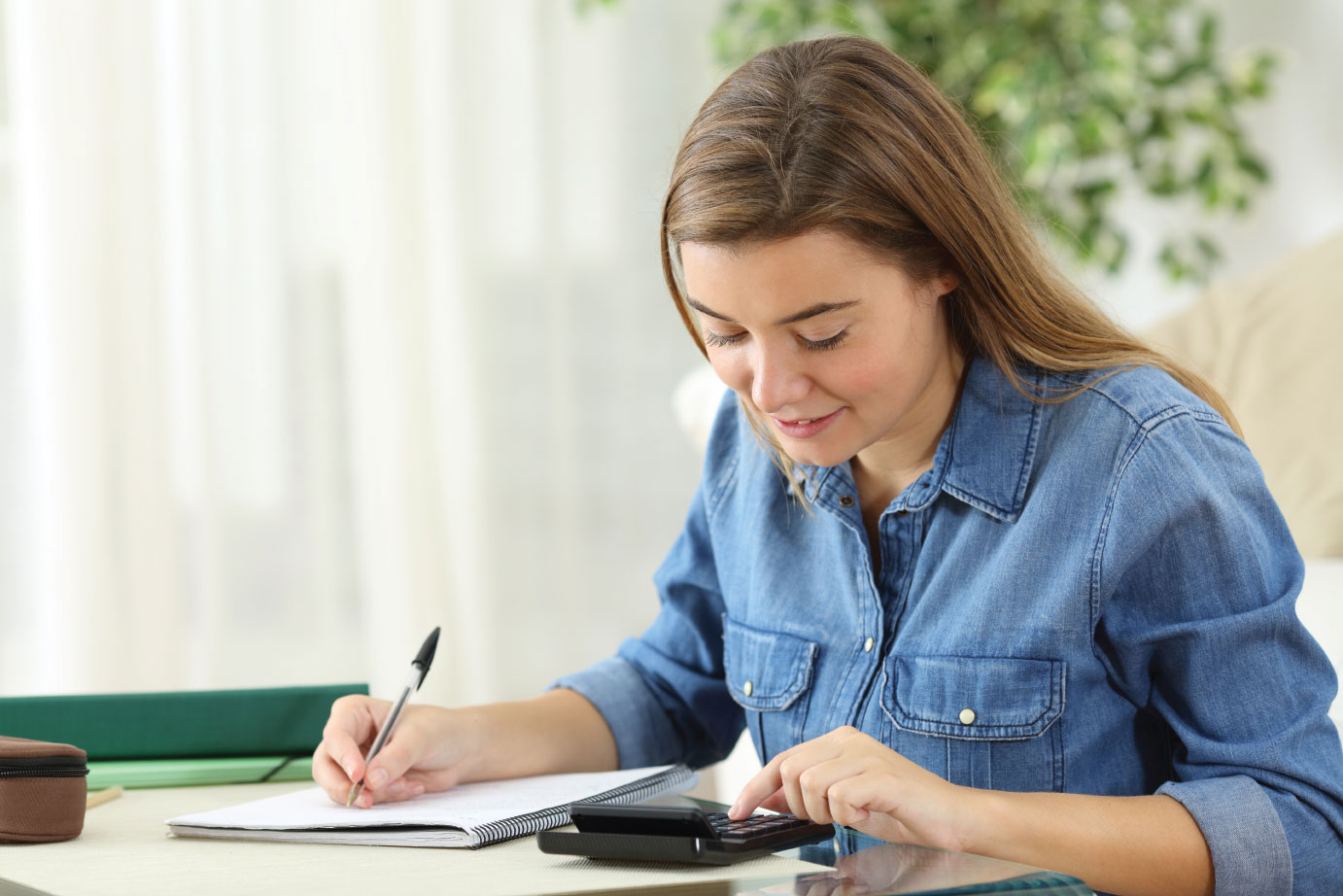 Student studying calculating with a calculator and handwriting notes siting on the floor in the living room at home